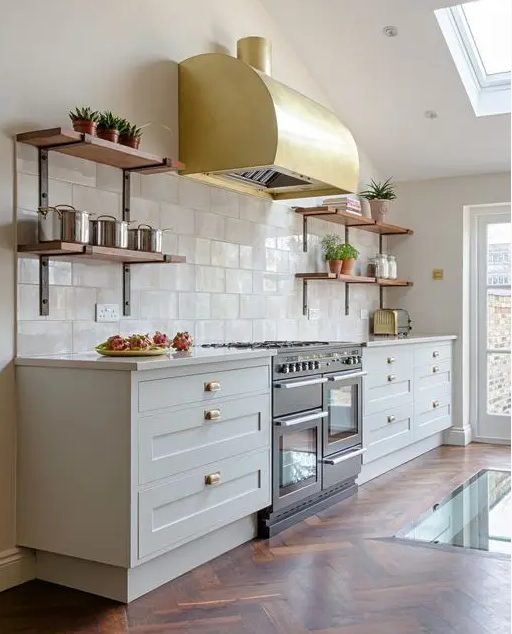 a lovely white kitchen with shaker cabinets, white stone countertops, a white Zellige tile backsplash and a glam gold hood