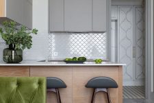 a minimalist kitchen with matte grey and stained cabinets, white countertops and a white fish scale tile backsplash, tall stools