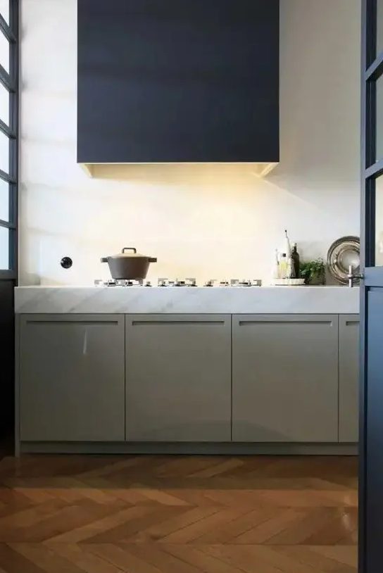a minimalist kitchen with olive green lower cabinets, a white stone countertop and a large black hood with lights