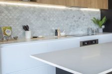 a minimalist kitchen with stained and white cabinets, white countertops, a marble scallop tile backsplash and lights