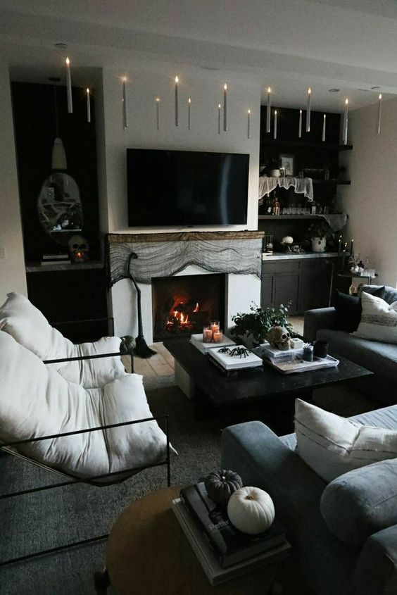a modern black and white Goth living room with a fireplace covered with cheesecloth, black and white pumpkins, white and black seating furniture and spiders