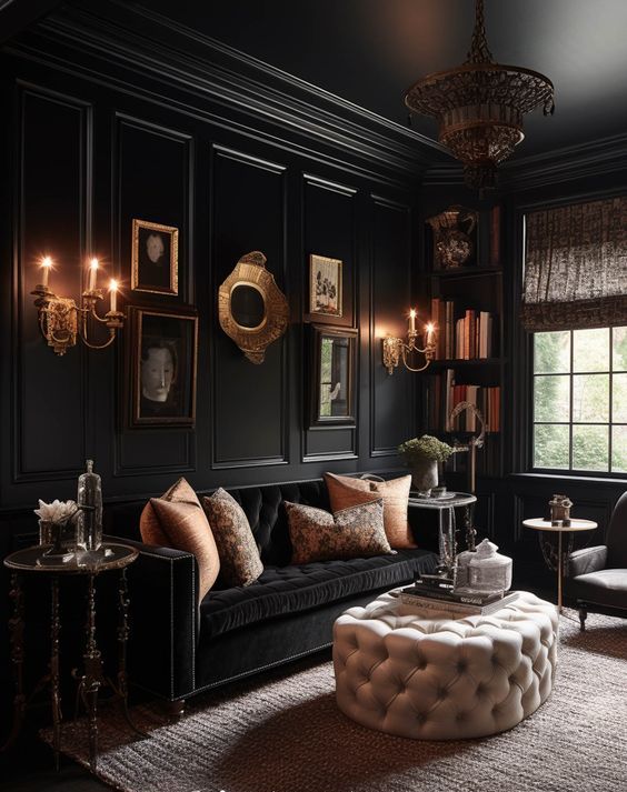 a modern Goth living room with black walls and a ceiling, a black sofa, gold pillows, a neutral ottoman, a gallery wall and a chandelier