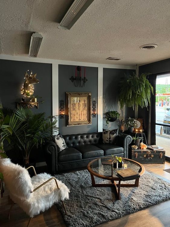 a modern Goth living room with soot walls, a black sofa, a white chair, a glass coffee table and potted plants