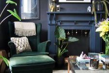 a modern Goth living room with soot walls, a navy fireplace, a green chair, shelves with decor, greenery and some art