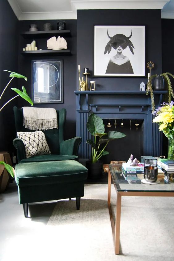 a modern Goth living room with soot walls, a navy fireplace, a green chair, shelves with decor, greenery and some art