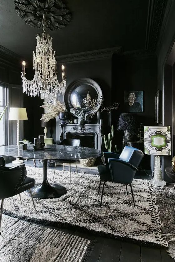 a modern Gothic dining room with black walls, floos and a ceiling, a stone table, leather chairs, mirrors, artworks and a refined chandelier