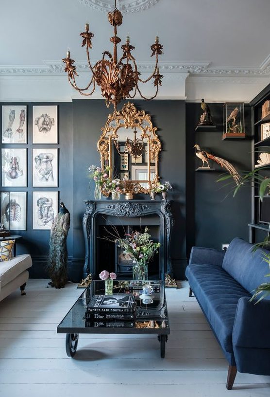a modern Gothic living room with black walls, a blue and white sofa, a fireplace, a refined chandelier and mirror, catchy artworks