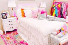 a modern and bright teen girl room with a bed with pink bedding and a bold pink rug, a makeshift closet, nightstands with lamps and a bench
