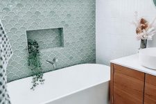 a modern bathroom clad with white stacked and green fish scale tile, an oval tub, a stained vanity and white appliances