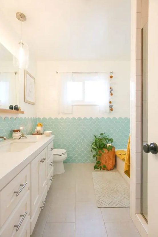 a modern beachy bathroom in neutrals, with aqua fishscale tiles, a tree stump, a large vanity and potted greenery