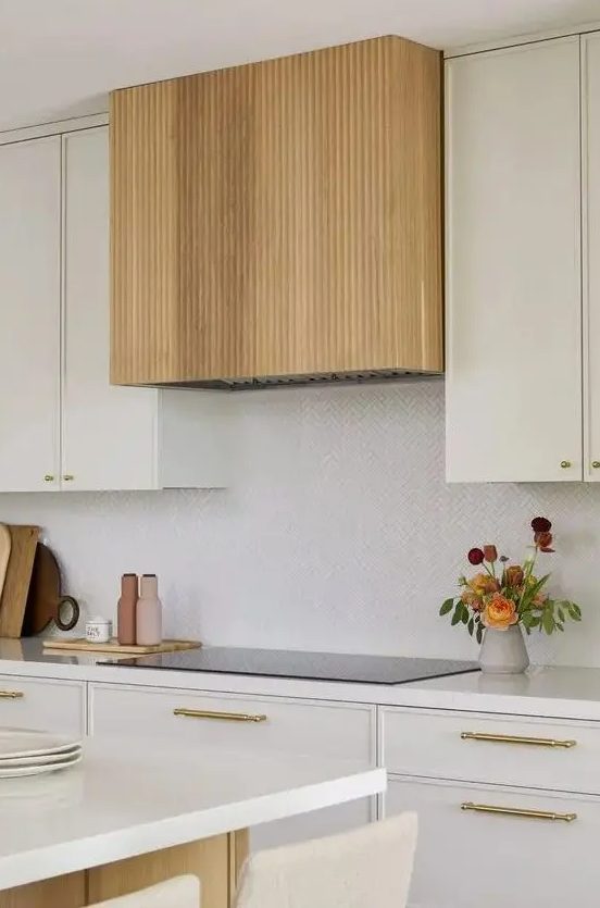 a modern creamy kitchen with gold fixtures and a fluted hood that accents the space and makes it look warm