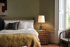 a modern earthy tone bedroom with green walls, a stained bed with catchy bedding,a  boucle bench and a geometric nightstand