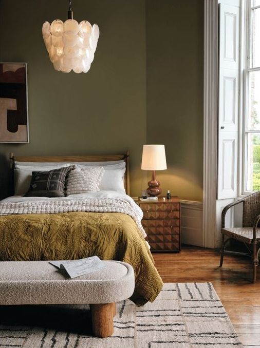 a modern earthy tone bedroom with green walls, a stained bed with catchy bedding,a  boucle bench and a geometric nightstand