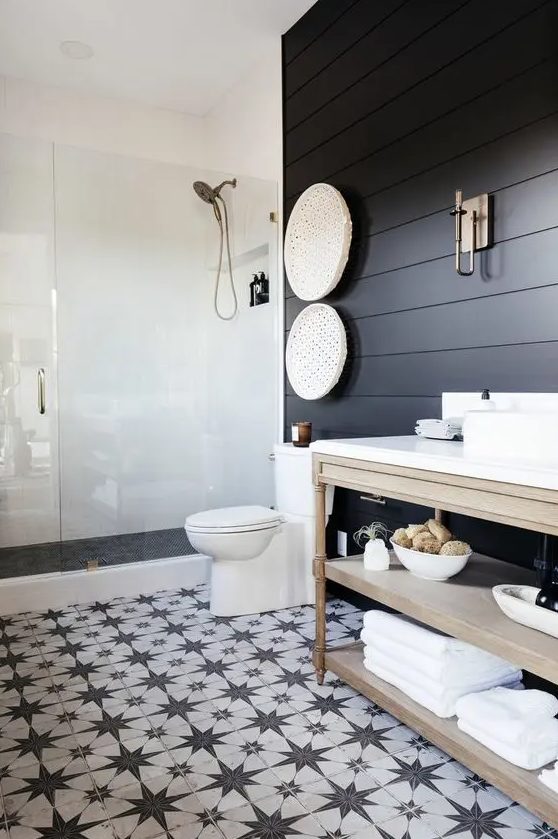 a modern farmhouse bedroom with soot shiplap walls, a shower space, a light stained vanity, a black and white star tile floor