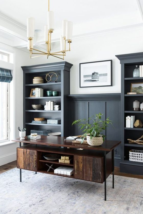 A modern farmhouse home office with soot cabinetry, a dark stained desk, decor, a potted plant and a gold chandelier