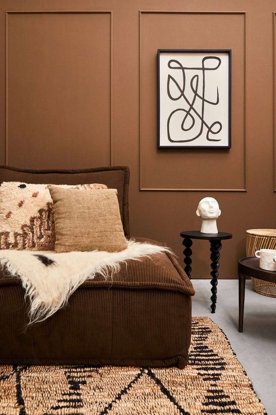 a modern living room with light brown walls, a brown sofa with pillows, tables and printed textiles