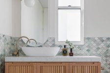 a modern sink space done with mermaid-inspired fish scale tiles, a fluted vanity, a sink, a cool pendant lamp