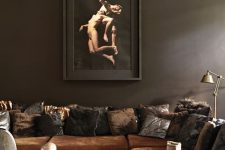 a moody and exquisite liivng room with dark brown walls, a rust-colored sofa and pillows, a coffee table and some lamps