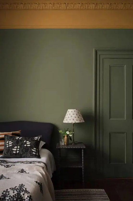 a moody bedroom with olive green walls and a mustard stucco ceiling, a black bed with printed bedding and a black nightstand