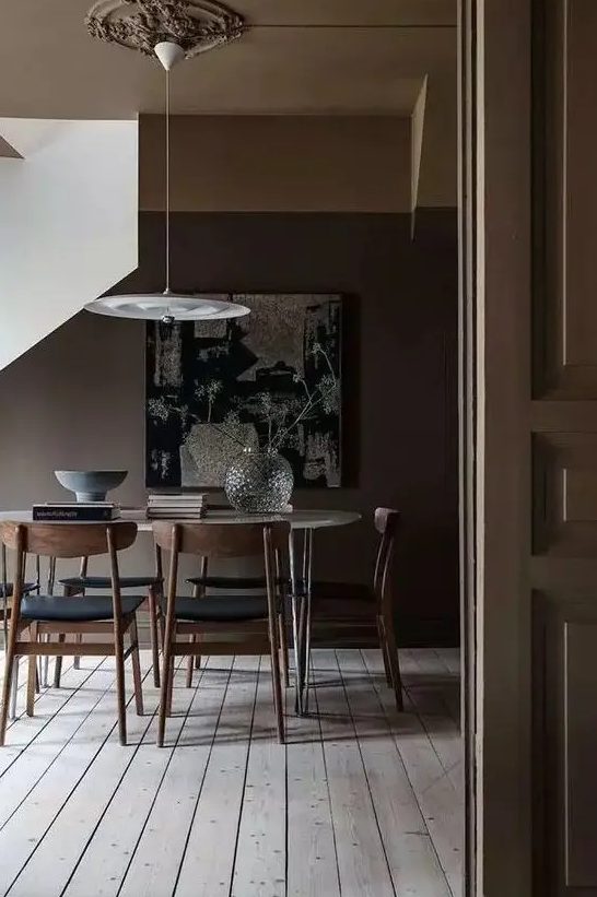 a moody deep brown dining space with a neutral floor, an oval hairpin leg table, black chairs and a pendant lamp