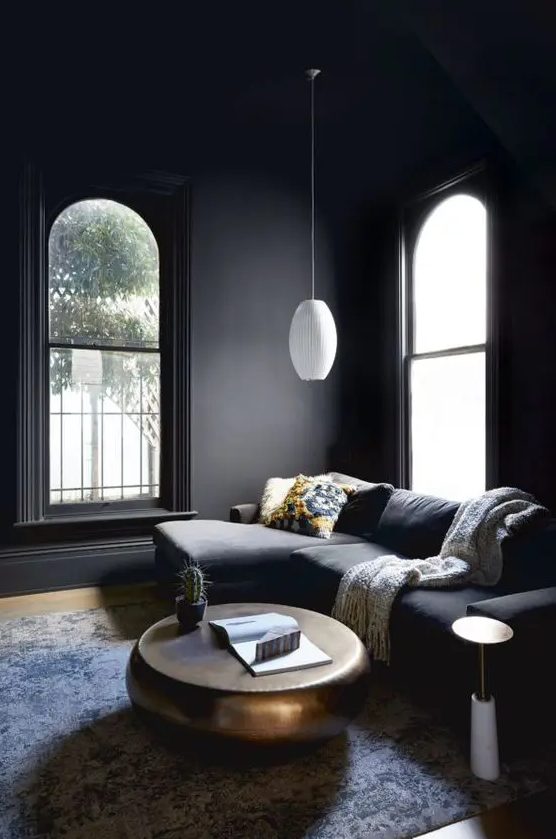 a moody living room with soot walls and a matching sectional, a metal coffee table and a white pendant lamp