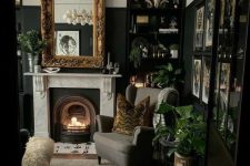 a moody modern Goth living room with a fireplace, a grey chair, built-in shelves with decor, a mirror in a gold frame, potted greenery