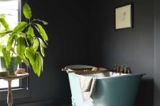 a moody soot bathroom with an aqua blue free-standing tub, a colorful rug, a potted plant and books and some art