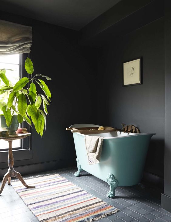 a moody soot bathroom with an aqua blue free-standing tub, a colorful rug, a potted plant and books and some art