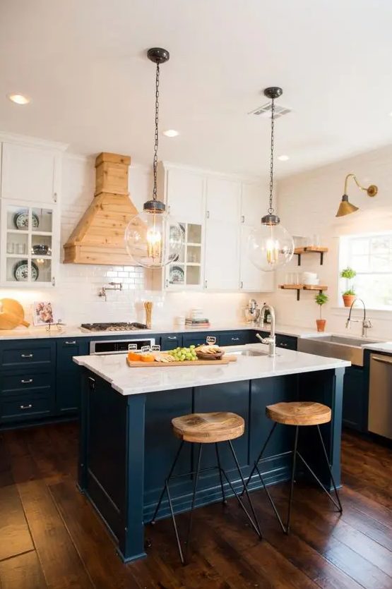 A navy and white kitchen with a white tile backsplash and countertops, a light stained wooden hood for an accent