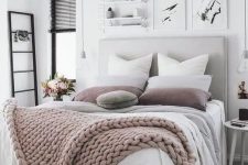 a neutral and pastel bedroom with a grey upholstered bed, layered blankets, black touches and bulbs hanging down