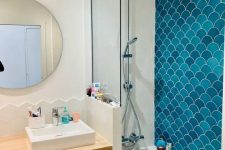 a neutral bathroom clad with white geo and blue fishscale tiles in the shower space, a vanity and a mirror and built-in lights