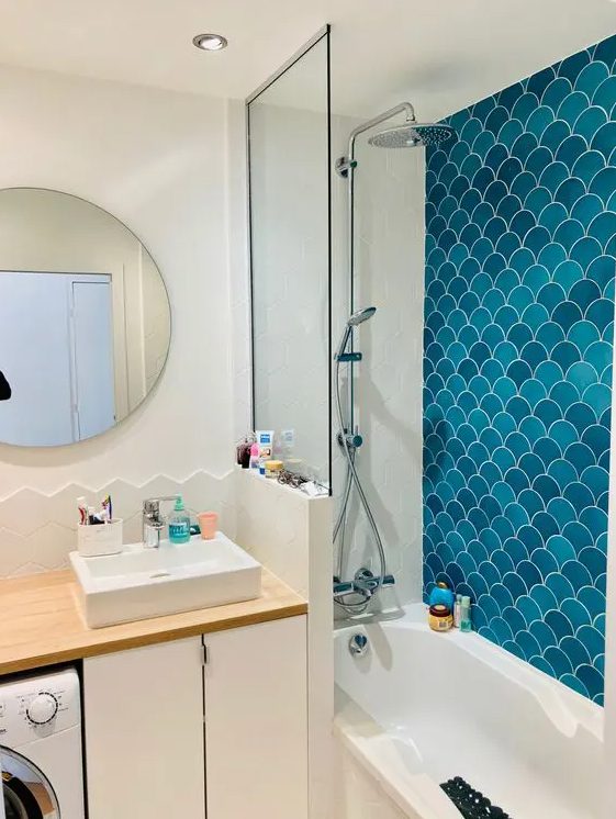 a neutral bathroom clad with white geo and blue fishscale tiles in the shower space, a vanity and a mirror and built in lights