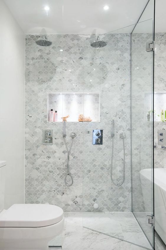 a neutral bathroom done with marble fish scale tiles, a shower and a tub, white appliances and built-in lights