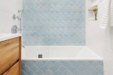 a neutral bathroom with white subway and blue fish scale tiles, a stained vanity, some niche shelves and some light