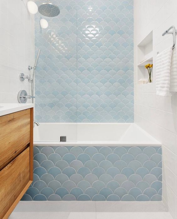 a neutral bathroom with white subway and blue fish scale tiles, a stained vanity, some niche shelves and some light