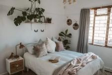 a neutral boho bedroom with a white forged bed with neutral bedding, nightstands, grey curtains, potted plants and a woven pendant lamp