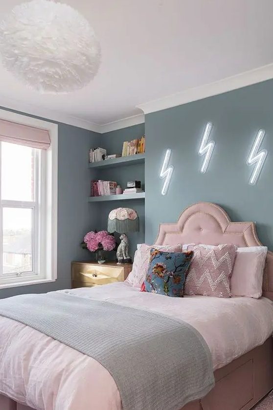 a pastel teen bedroom with blue walls, a pink bed with pastel bedding, built-in shelves, a stained dresser and blush curtains