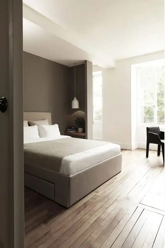 a pretty and laconic bedroom with a niche for sleeping, a taupe accent wall and a taupe bed here, a small nightstand and a pendant lamp plus a black chair