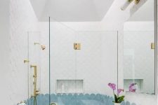 a pretty bathroom done with white and blue scallop tiles, a white vanity, a mirror and gold fixtures is chic and cool