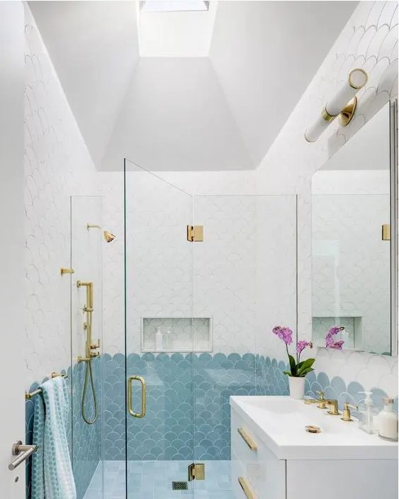 a pretty bathroom done with white and blue scallop tiles, a white vanity, a mirror and gold fixtures is chic and cool