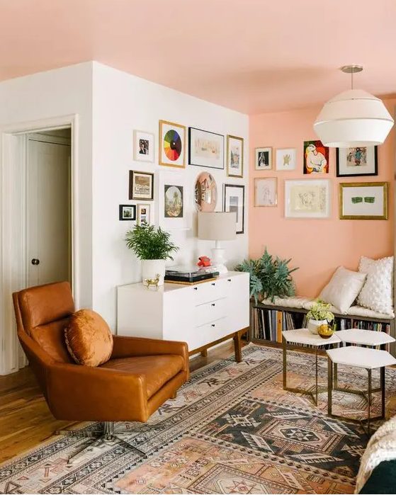 a pretty mid-century modern living room with a Peach Fuzz wall and ceiling, a bench with books, a white credenza, a leather chair