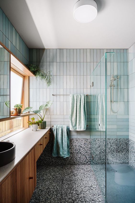 a quirky bathroom clad with aqua and grey stacked tiles and terazzo floor, a stained vanity and potted greenery