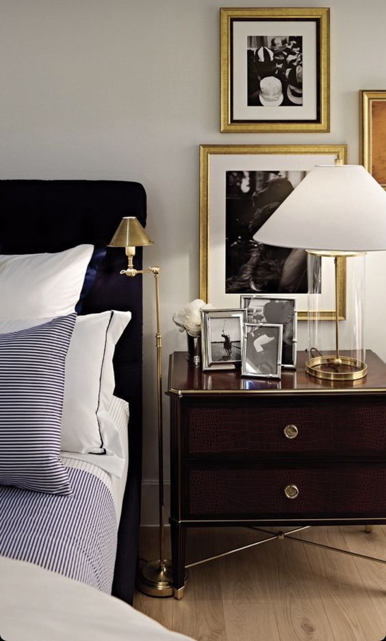 A refined bedorom with a navy upholstered bed and printed bedding, a dark stained nightstand and gold touches