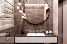 a refined brown bathroom with tiles, built-in lights, pendant lamps and a round mirror
