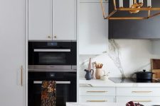 a refined contemporary white kitchen with a white stone backsplash and countertops plus a large black hood and a pendant lamp