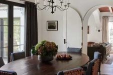 a refined dining room with an oval dark-stained table, black woven chairs, potted greenery and a vintage chandelier