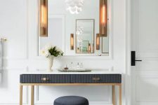 a refined entryway with a large mirror, a soot vanity with a ribbed surface, a soot pouf and chic sconces