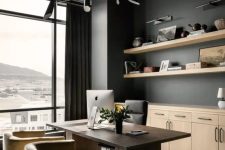 a refined home office with soot walls, a glazed wall, a dark-stained desk, neutral and a black chair, a black chandelier and light-stained cabinets