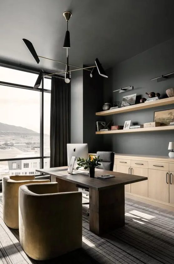 a refined home office with soot walls, a glazed wall, a dark stained desk, neutral and a black chair, a black chandelier and light stained cabinets