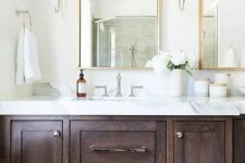 a refined neutral bathroom with a dark-stained vanity, a white stone countertop, mirrors in gilded frames and neutral sconces